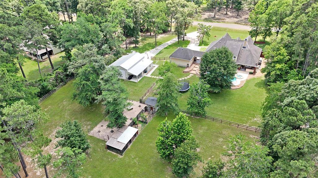 A drone shot from above the rear of the property highlights the full extent of the estate’s features: a pool with integrated spa, detached workshop with 1/2 bath, chicken coop, and fenced pastures. There's room to live, play, garden, or raise animals—all within a private, tree-lined oasis.