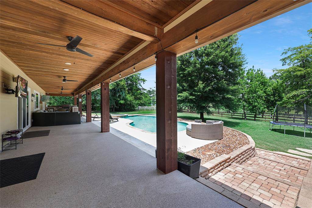 This expansive covered patio with epoxy concrete flooring with grit for a non-slip surface features a wood ceiling, outdoor ceiling fans, recessed and string lighting—perfect for relaxing or entertaining in style. Enjoy views of the lake and pool while lounging under the shade or watching the game one of the two wall-mounted TVs.