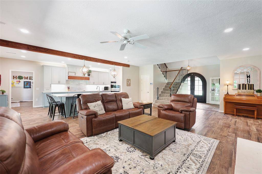 This photo highlights the effortless flow between the living area and gourmet kitchen. A rustic wood beam adds character above the breakfast bar, while pendant lights bring a touch of elegance. The room’s layout is ideal for both relaxed evenings and entertaining, with views of the front entryway and staircase completing the warm, welcoming atmosphere.