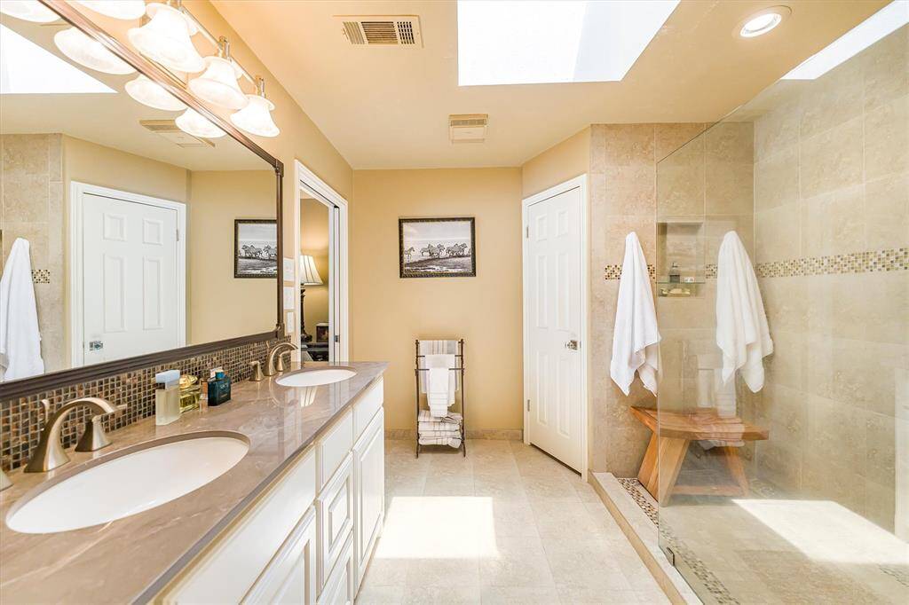 His & her closets, private toilet area with storage, double sinks, dirty laundry closet, and large tile shower.