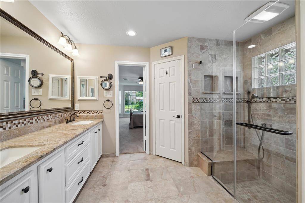 Modern primary bath featuring glass-walled shower, double sinks, and large mirror.