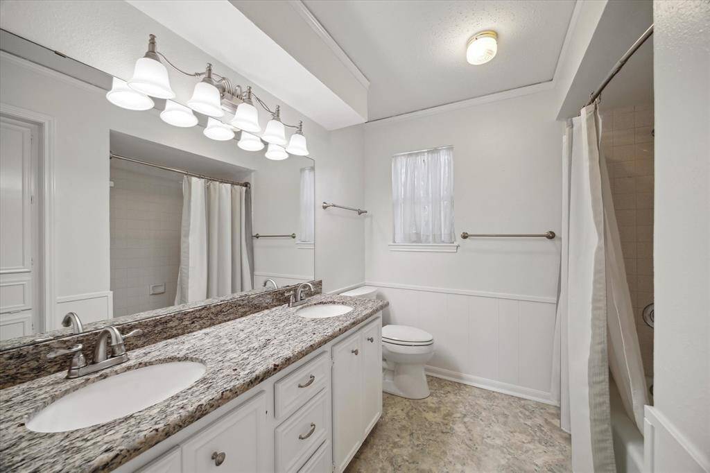 Full bath featuring a tub-shower combo, dual sinks, big mirror, and storage cabinets.