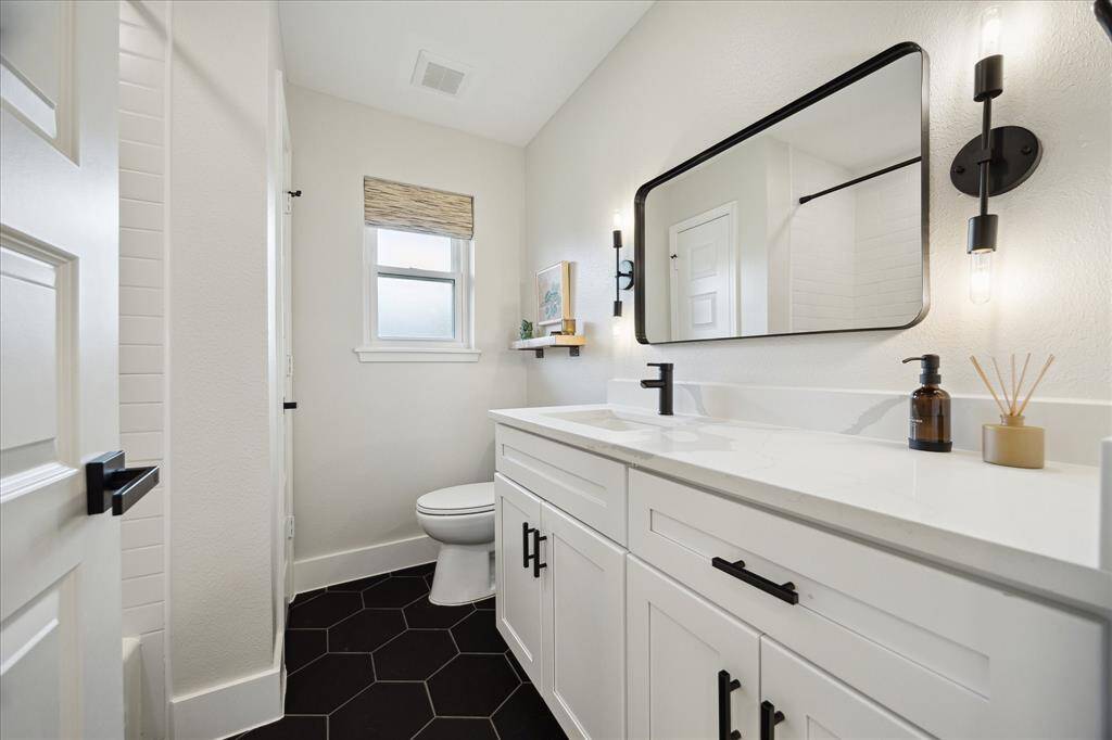 Thoughtfully updated SECONDARY BATH with quartz countertops, and modern sconces framing the mirror. A small window with a privacy shade.