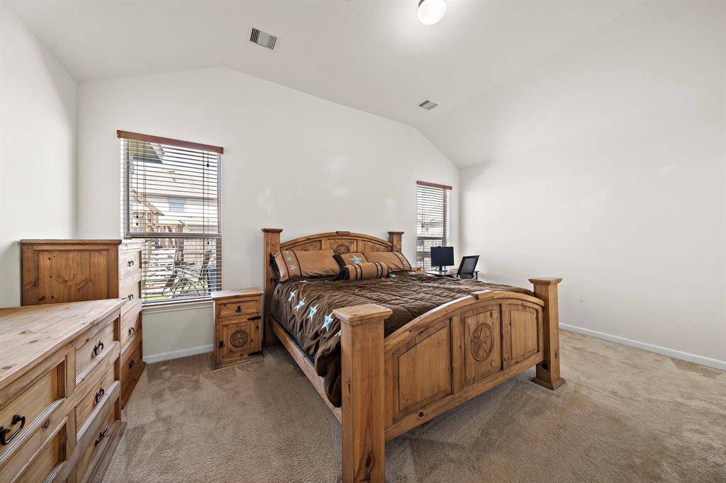 This spacious bedroom features high ceilings, two large windows for natural light, and rustic wooden furniture, creating a warm and inviting atmosphere.