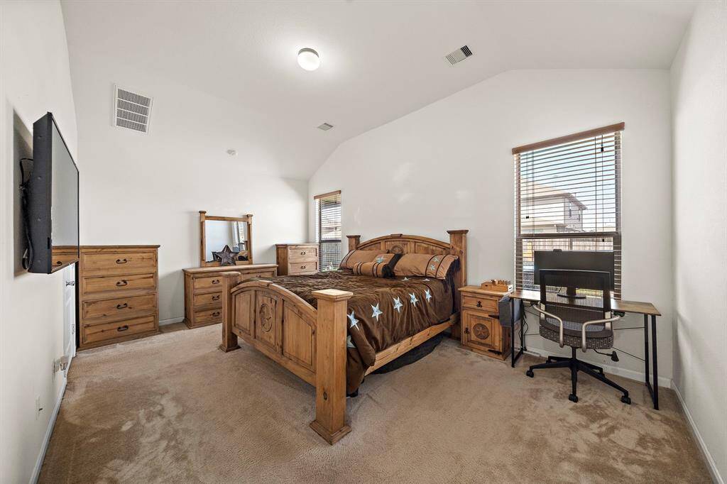 This spacious bedroom features high ceilings and ample natural light from large windows. It includes a wooden bed frame, matching dressers, and a desk, offering both comfort and functionality.