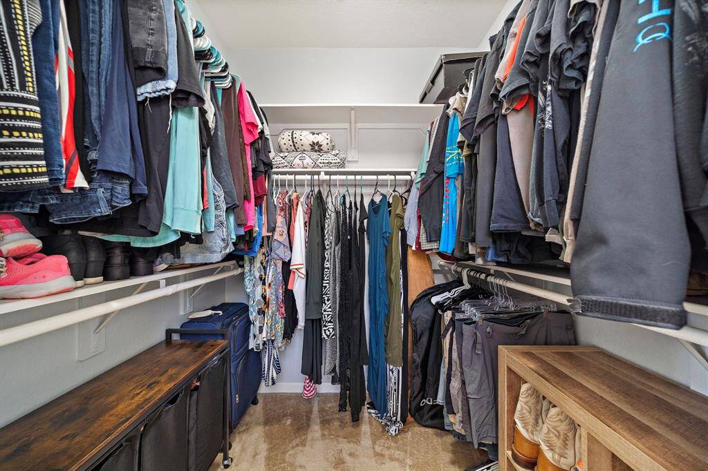 This photo showcases a spacious walk-in closet with ample hanging space, shelves, and storage options. The closet is organized with clothing, shoes, and accessories, offering a practical and efficient storage solution.
