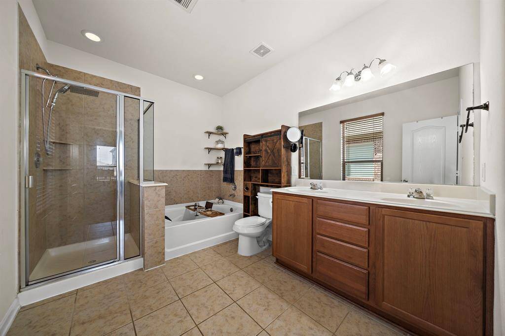 This bathroom features a spacious layout with a glass-enclosed shower, separate bathtub, and double vanity with ample storage. Neutral tiles and modern fixtures create a clean, inviting atmosphere.