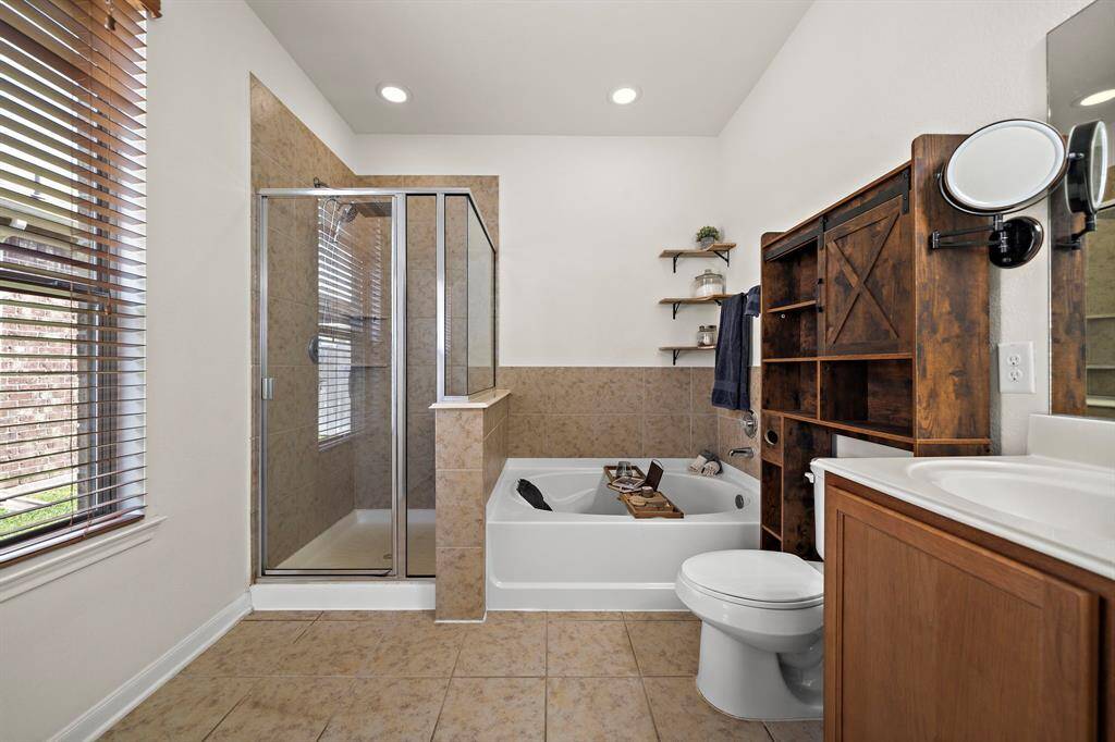 This bathroom features a spacious walk-in shower, a soaking tub, and stylish wooden cabinetry. It has tiled flooring, a large window for natural light, and modern fixtures, creating a warm and inviting space.