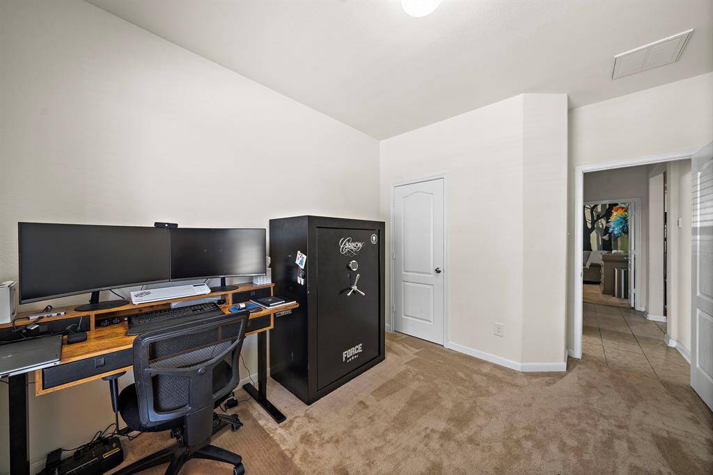 This bedroom that is the front of the house has a view to any guest arriving and is currently being used as a home office has neutral walls, carpeting, and a small walk-in closet.