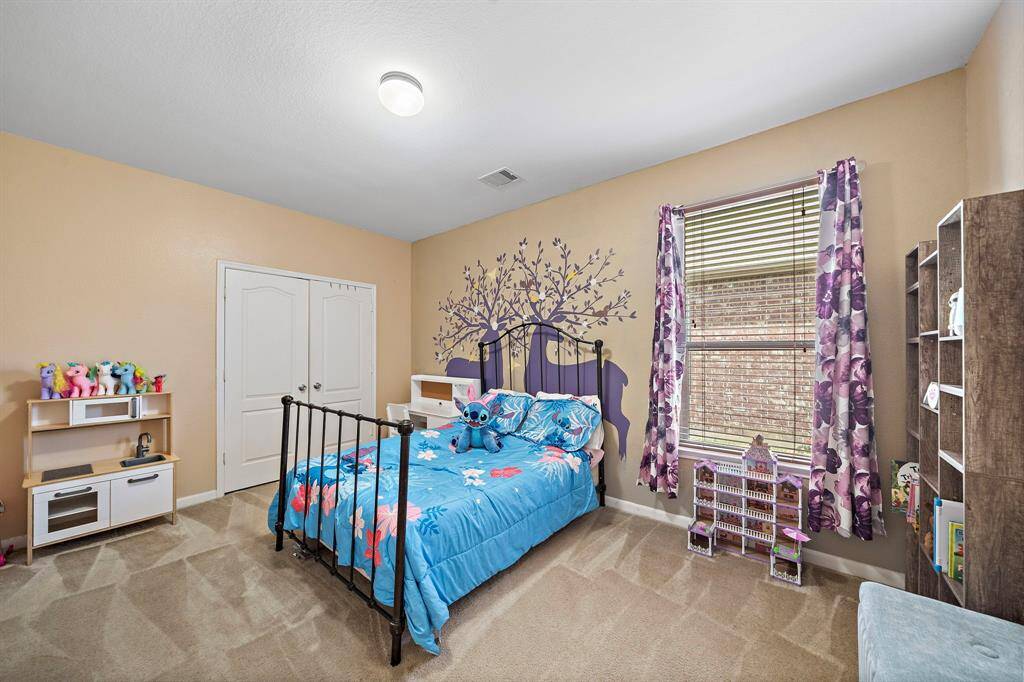 Cozy children's bedroom featuring a whimsical tree mural, single bed with vibrant bedding, and playful decor. It includes a small play kitchen, ample natural light from a window with floral curtains, and a closet with double doors.