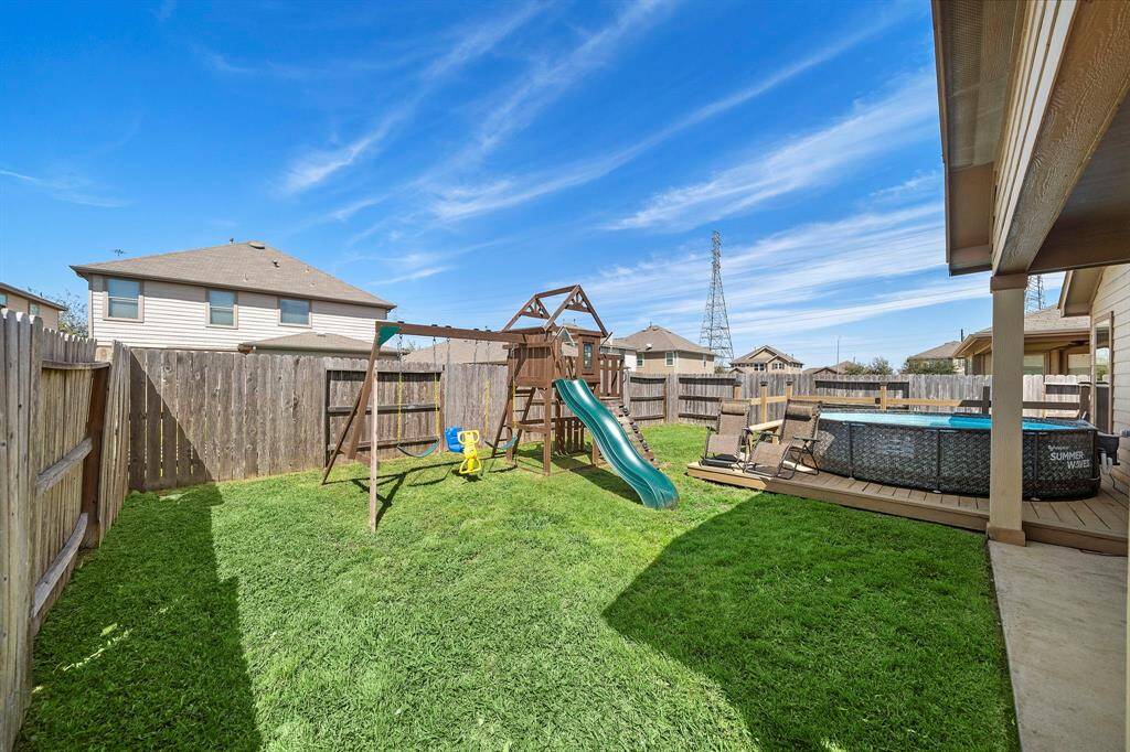 Spacious backyard featuring a playset with swings and slide, a fenced perimeter for privacy, and an above-ground pool with a deck for relaxation and family fun.