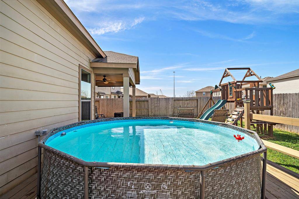 The backyard features a round above-ground pool next to a covered patio. There's also a wooden playset with slides, all enclosed by a privacy fence, offering a family-friendly outdoor space.