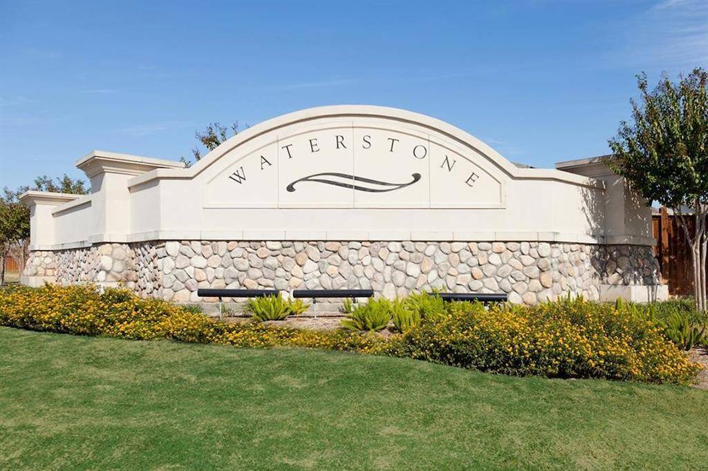 The photo shows an elegant entrance sign for "Waterstone," featuring a stone and stucco design surrounded by well-maintained landscaping. Perfect for a welcoming community atmosphere.