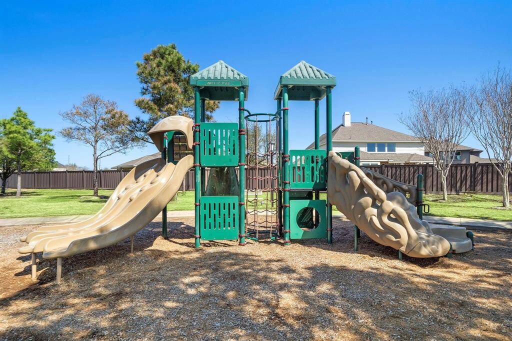 A neighborhood well-maintained playground with slides and climbing structures, set in a grassy area with trees and nearby houses, ideal for families.