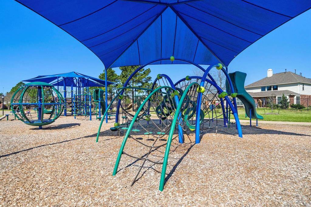 Another Larger view of a neighborhood playground with shaded climbing structures and slides, surrounded by wood chips. It's ideal for families, and friends.