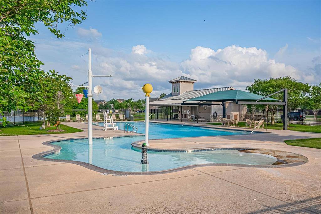 The community pool area with a children's splash pad, a large swimming pool, shaded seating, and well-maintained surrounding greenery.