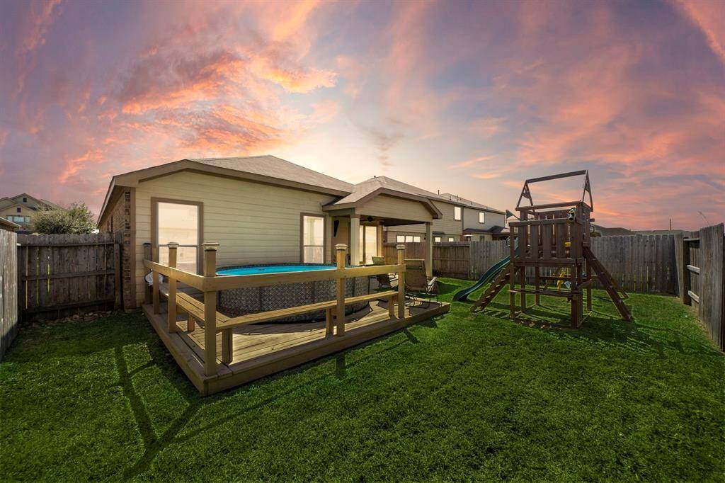 Charming backyard with a wooden deck and an above-ground pool is enclosed by a wooden fence, offering privacy and a safe play area. Beautiful sunset sky adds to the serene atmosphere.