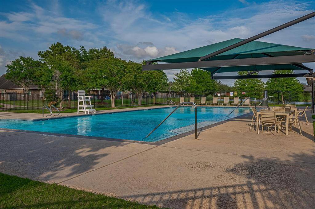 The well-maintained community pool area with a large swimming pool, shaded seating, and surrounding greenery, offering a great space for relaxation and recreation.