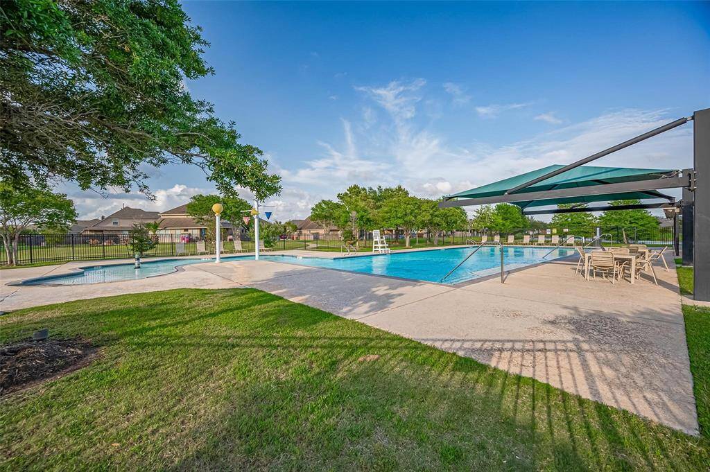 Another Large view of this a spacious outdoor community pool area with a sunshade, surrounded by greenery and seating.