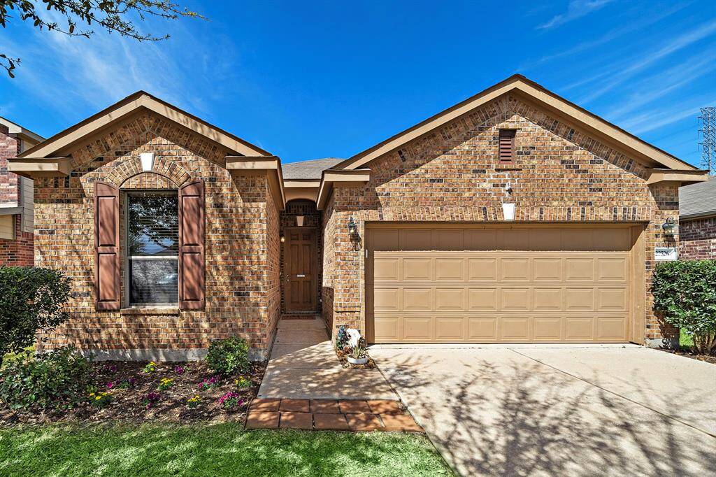 This is a charming brick home with a neatly landscaped front yard and a two-car garage. The property features a welcoming entrance with a wooden front door, accented by a flower bed and shutters on the window. The exterior is well-maintained, offering great curb appeal.