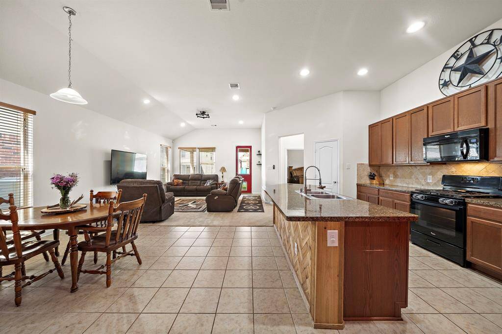 This spacious open-concept living area features a modern kitchen with granite countertops and a central island, flowing into a cozy living room with ample natural light. Ideal for entertaining, it also includes a dining area with tile flooring.