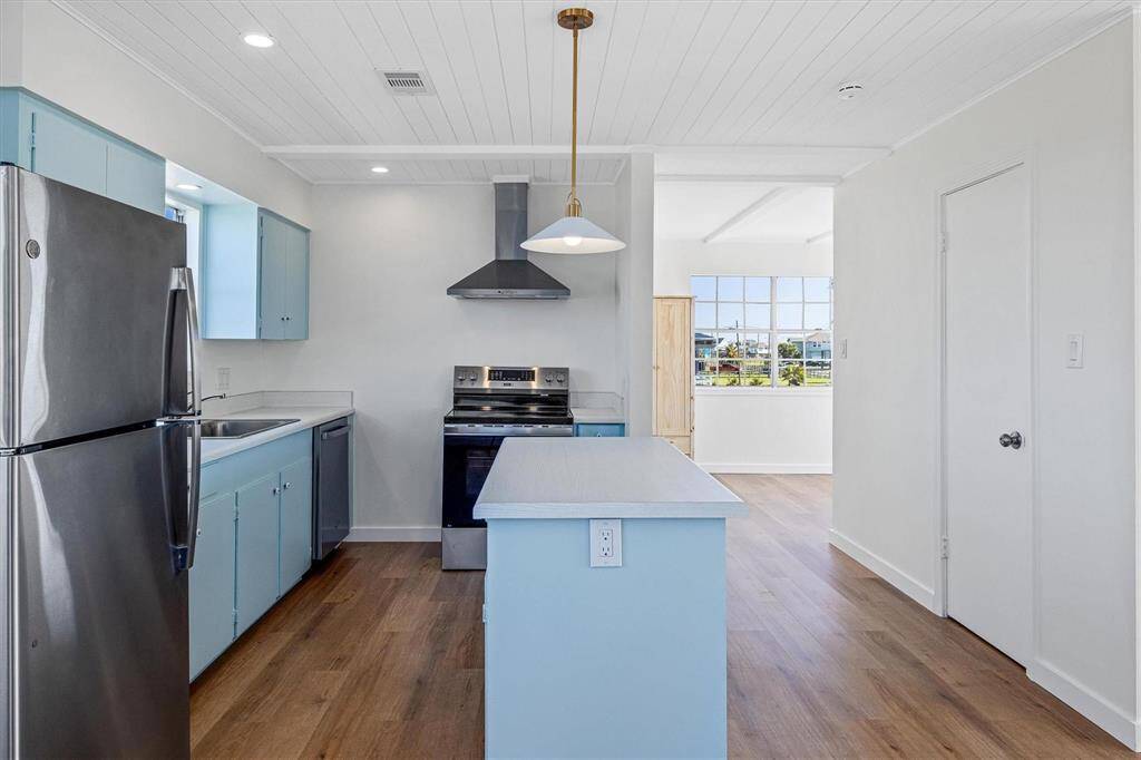 Kitchen featuring dark wood-type flooring, blue cabinetry, wall chimney exhaust hood, and stainless steel appliances