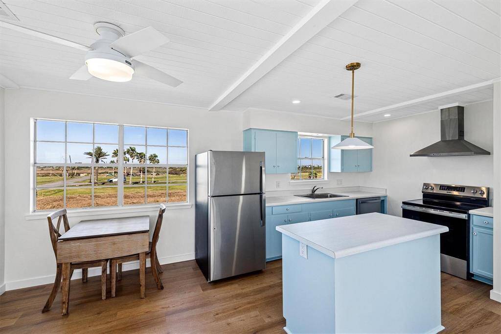 Kitchen with wall chimney range hood, light countertops, appliances with stainless steel finishes, blue cabinets, and a sink