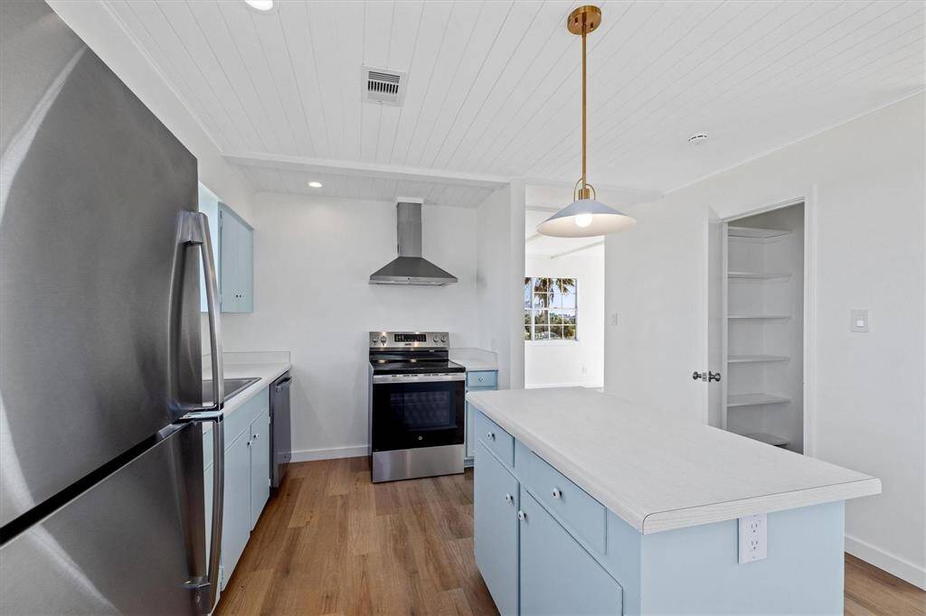 Kitchen featuring blue cabinetry, wall chimney exhaust hood, visible vents, and appliances with stainless steel finishes