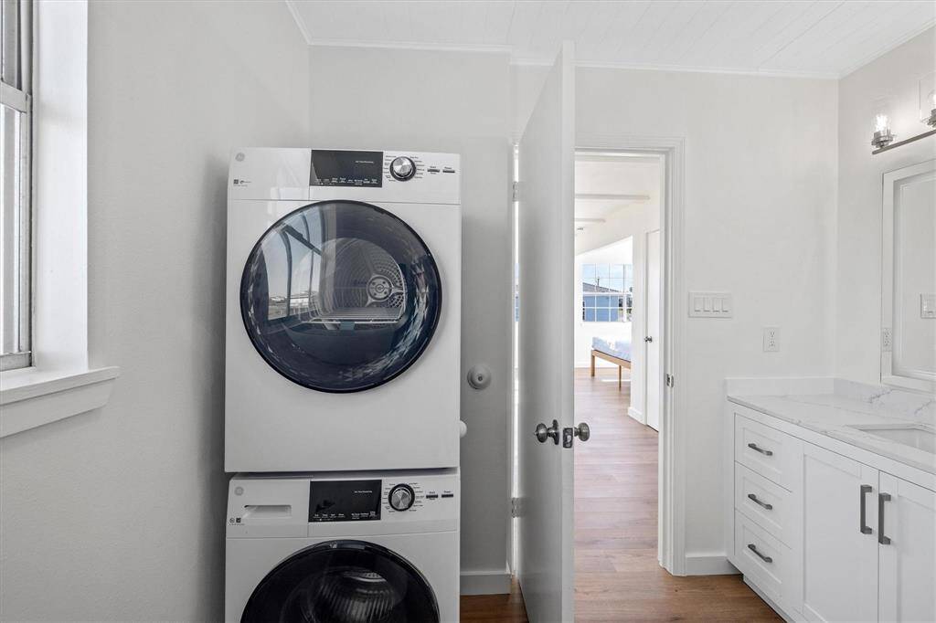 Washroom featuring laundry area, stacked washer and dryer, wood finished floors, and crown molding