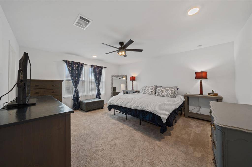 Upstairs spacious primary bedroom offers natural light through large windows and features a ceiling fan for added comfort.