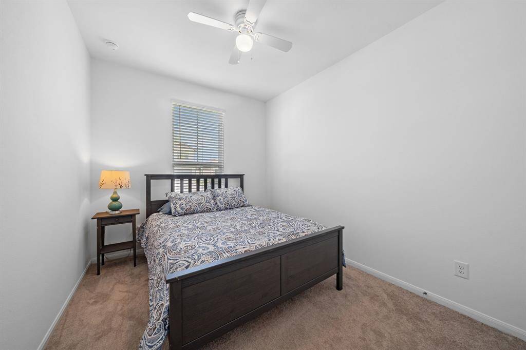 This bedroom with an ensuite bath features white walls and a white ceiling fan, creating a clean and bright atmosphere.