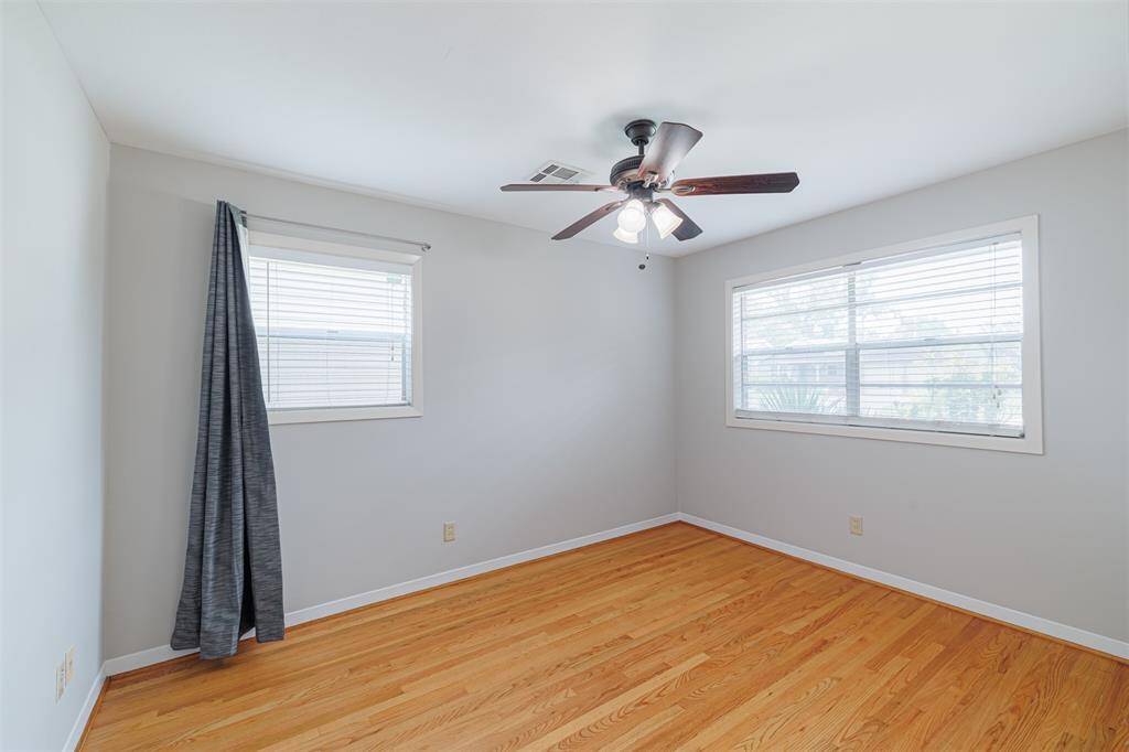 First bedroom with ceiling fan, hardwood floors, and large windows that bring in natural light.