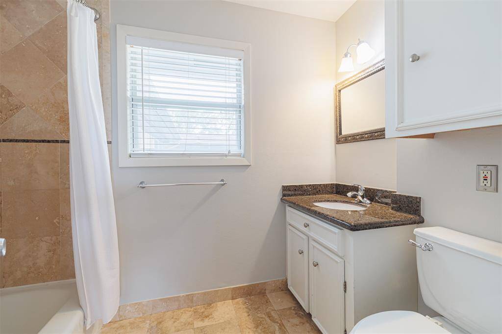 This bathroom features a granite countertop, under-mount sink.  It includes a bathtub with a tile surround and a window for natural light.