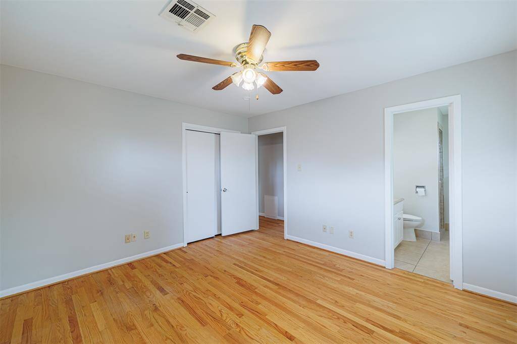 Bright bedroom with hardwood floors, a ceiling fan, neutral walls, and an ensuite bathroom. Features a closet with double doors.