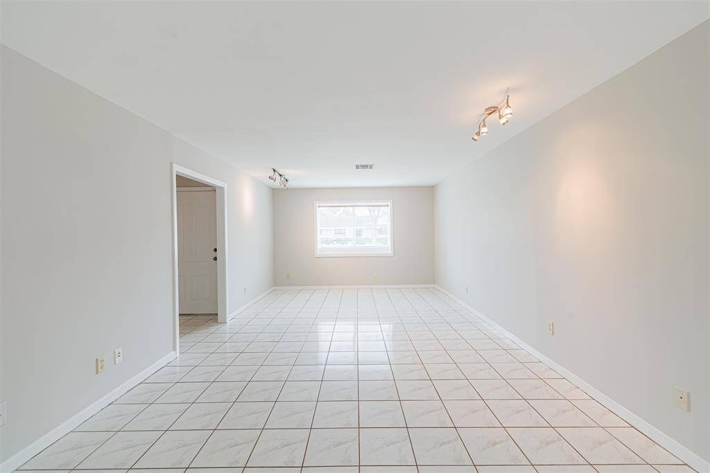 Spacious, well-lit room with neutral colors and tiled flooring. Features a large window, ceiling lights, and an open entryway. Perfect for versatile use.