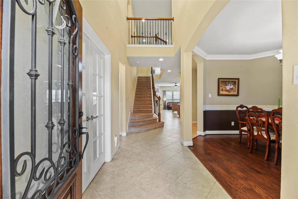 Step through the elegant leaded glass door adorned with intricate iron accents into a welcoming foyer where gleaming tile floors stretch beneath soaring ceilings. Crown molding adds a touch of timeless sophistication, setting the tone for the refined beauty that unfolds throughout the home.