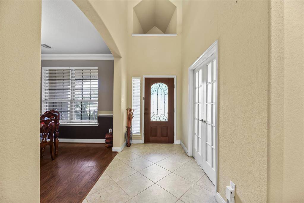 Above the front door, an art niche offers a perfect showcase for a statement piece, drawing the eye upward and adding a custom touch of elegance. Just beyond, glass double doors lead into the home office, allowing natural light to flow through while maintaining a sense of openness and refined distinction.