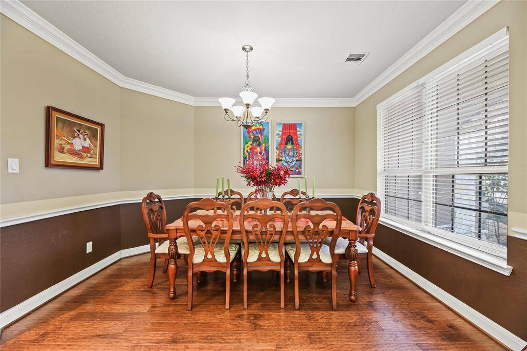 The elegant dining room features rich wood floors and classic chair rail molding that adds depth and dimension to the space. Crown molding gracefully frames the ceiling, while a sparkling chandelier serves as a stunning centerpiece, casting a warm, inviting glow perfect for gatherings and special occasions.