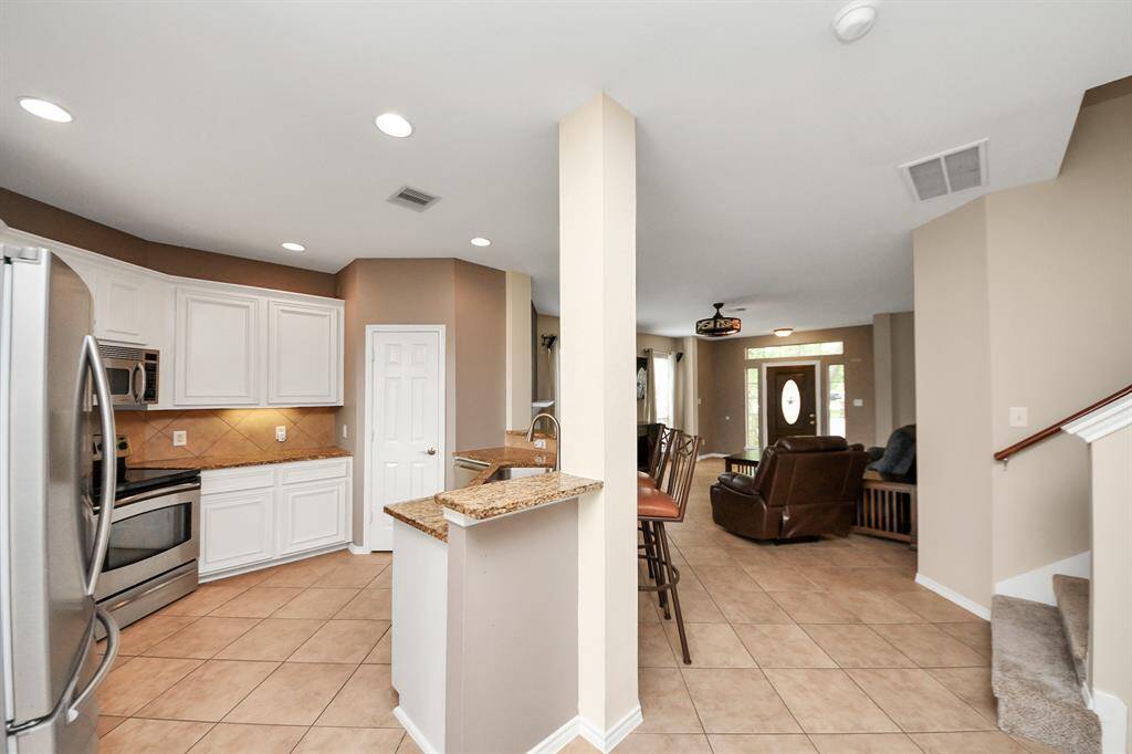 Clean lines and timeless finishes define the kitchen, where white cabinetry meets sleek granite countertops. A breakfast bar overlooks the living area, blending function and openness.