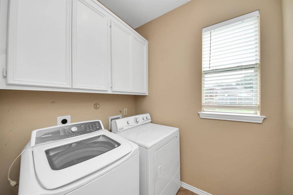 A practical space, the laundry room includes overhead cabinetry for storage and a cheerful window that brightens daily routines.