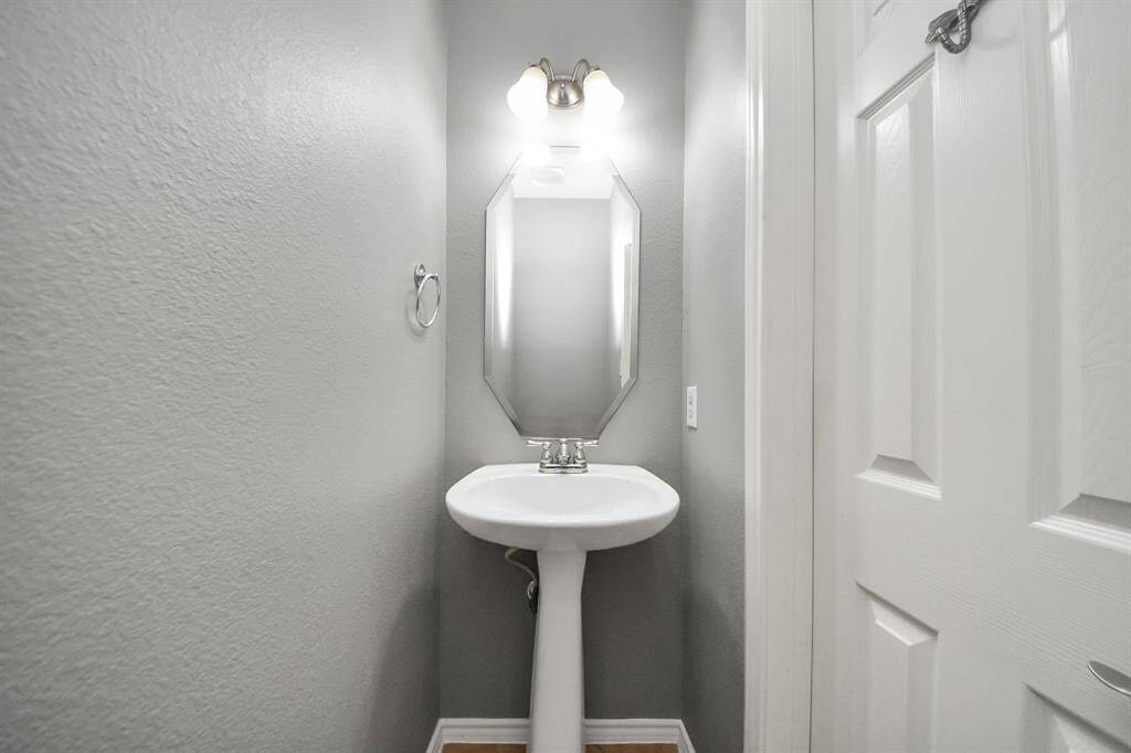 The half bath pairs simplicity with style—featuring a pedestal sink, a frameless mirror, and crisp lighting that enhances the clean, uncluttered design.