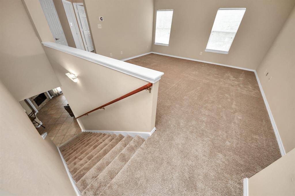 Carpeted stairs lead to a generous upstairs landing, where a game room awaits with large windows. Ideal for creative use—study area, media lounge, or a quiet corner to unwind.