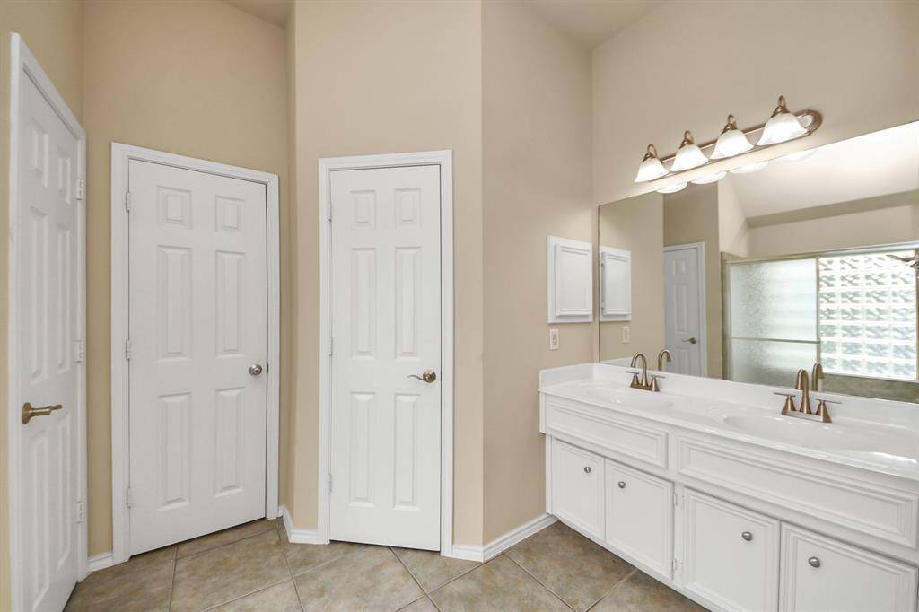 The en suite bath includes a dual-sink vanity, wide mirror, and a shower with an upgraded closure, highlighted by a stunning glass block window for both privacy and natural light.