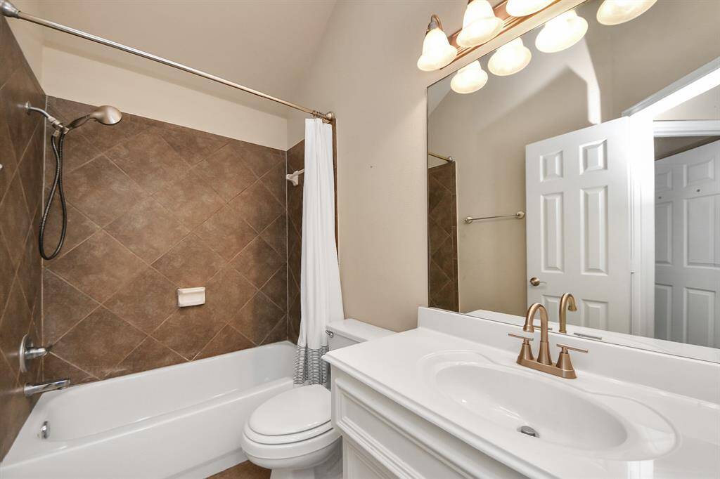A tiled shower-tub combo is the highlight of this full bathroom, paired with a clean vanity and warm tones for a soothing ambiance.