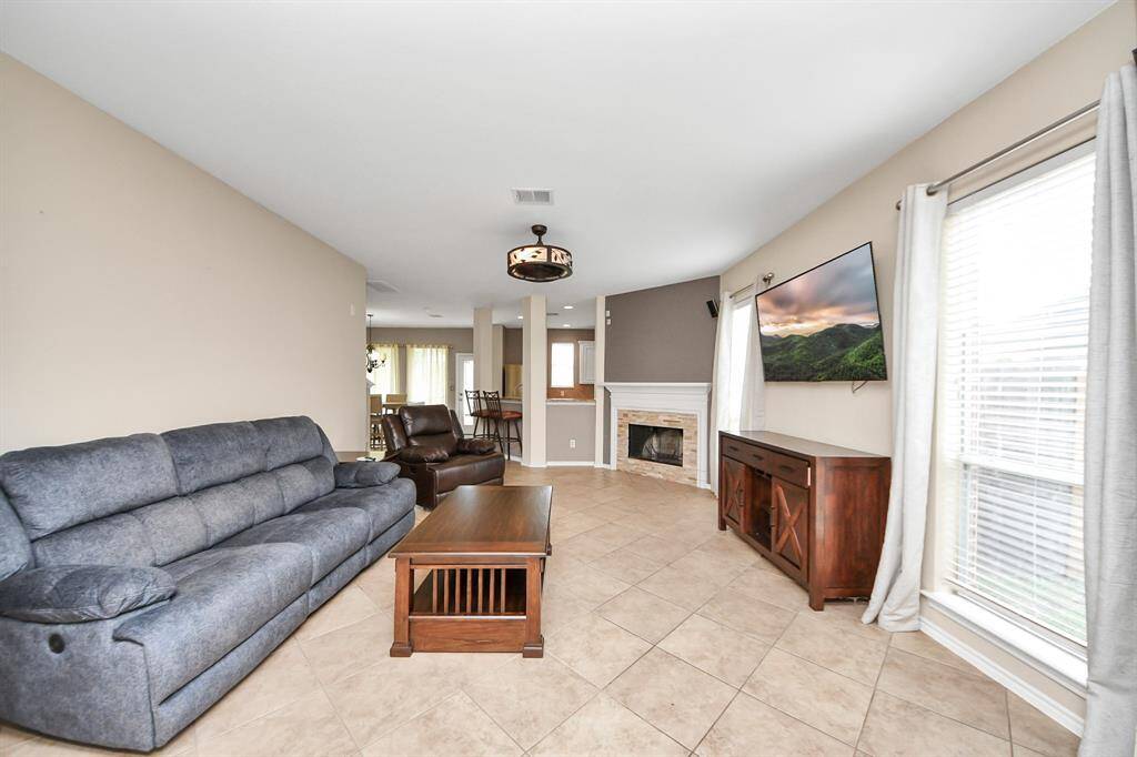 Step inside to a bright and airy living room, anchored by a gaslog fireplace and tall windows that invite in soft natural light. The space opens gracefully to the kitchen further within.
