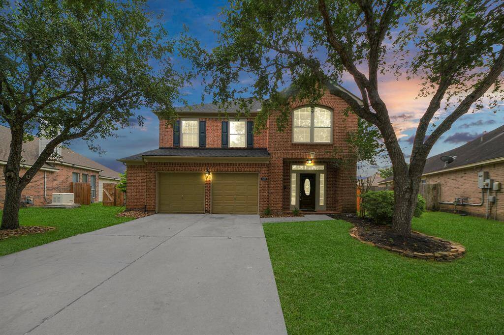 As the sun sets, the home glows with warmth. Twilight paints the sky in soft hues, casting a golden light behind the brick façade and welcoming entry.