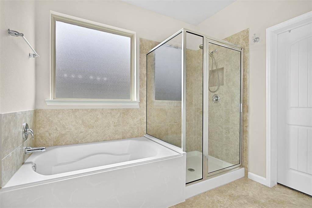 The primary bath also features a soaking tub beneath a privacy-glass window and a separate glass-enclosed shower with tile surround.