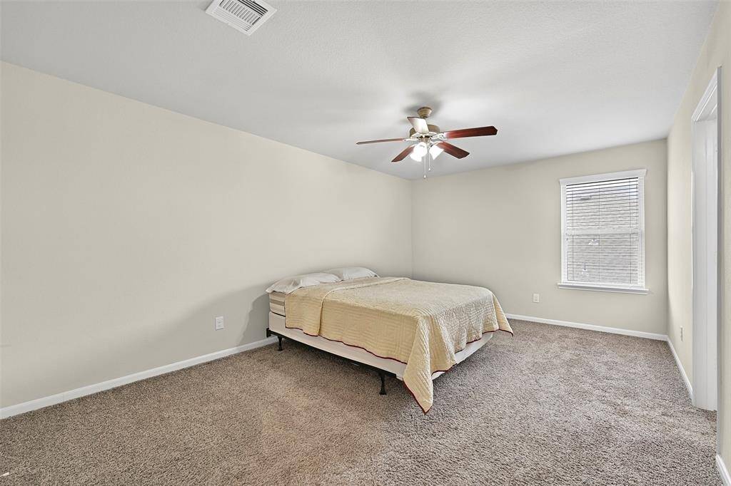 The first of three spacious upstairs secondary bedrooms features fresh neutral paint, plush carpet, a side-facing window shaded by 2 -inch blinds, a private en suite bathroom, and a large walk-in closet for ample storage.