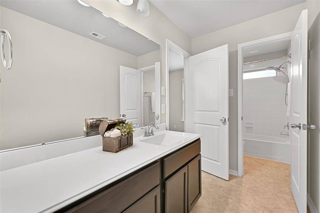 The private en suite bathroom features a lengthy cultured marble vanity with a rectangular basin sink and espresso cabinetry, modern lighting, tile floors, and a separate tub/shower combo with a classic white tile surround.