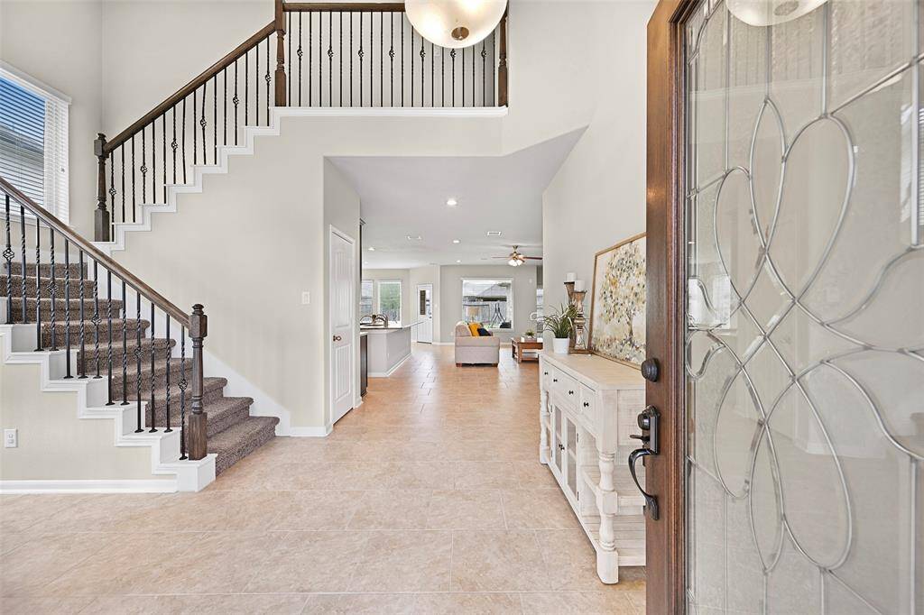 Step through the decorative leaded glass & wood front door into a welcoming foyer with soaring ceilings, durable tile flooring, and a split staircase with wrought iron spindles that sets the tone for the stylish and functional layout beyond.
